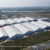 Vista aérea de um grande complexo de tendas de exposição com estrutura de alumínio, onde se realiza uma exposição mundial