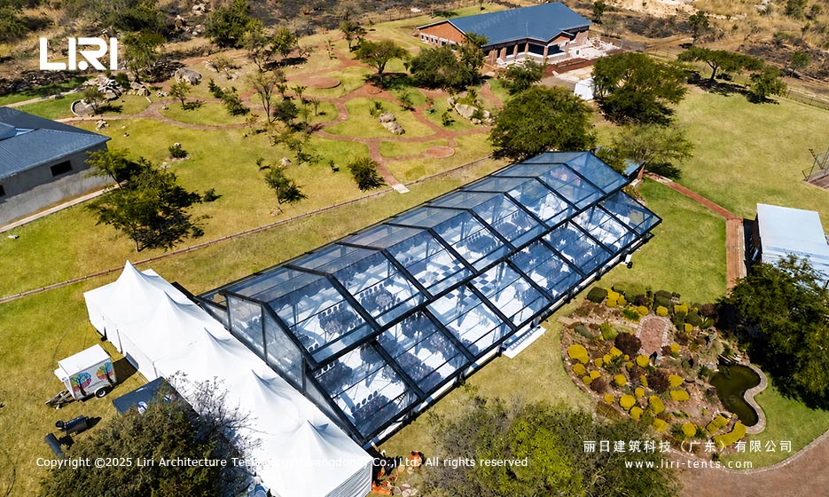 Vista aérea de uma tenda tipo orangerie para eventos ao ar livre, com telhado transparente e cenário de jardim